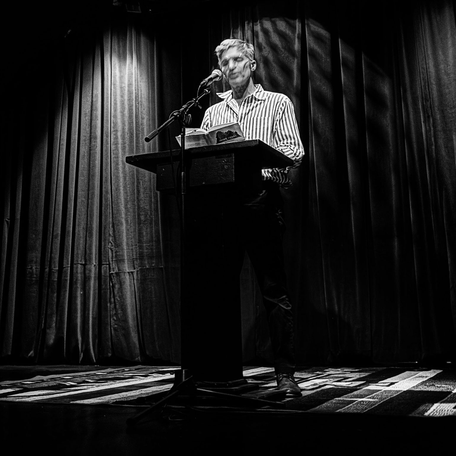 Blas Falconer reading at the podium on the Wanda Coleman Theater stage